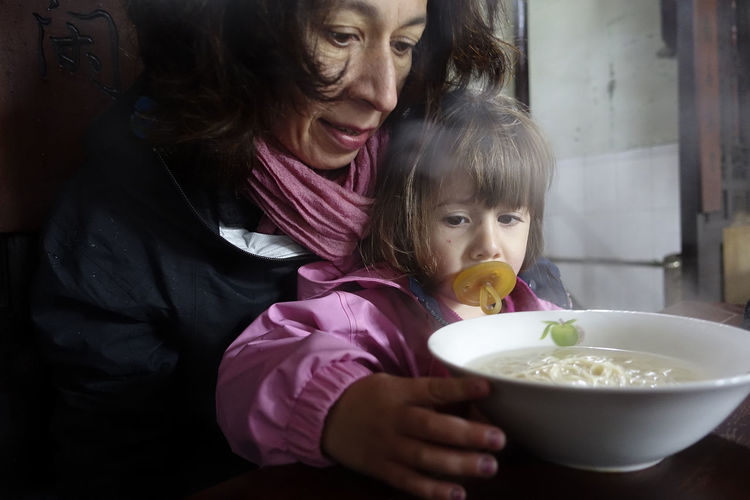 Mother and daughter holding noodles in bowl at home