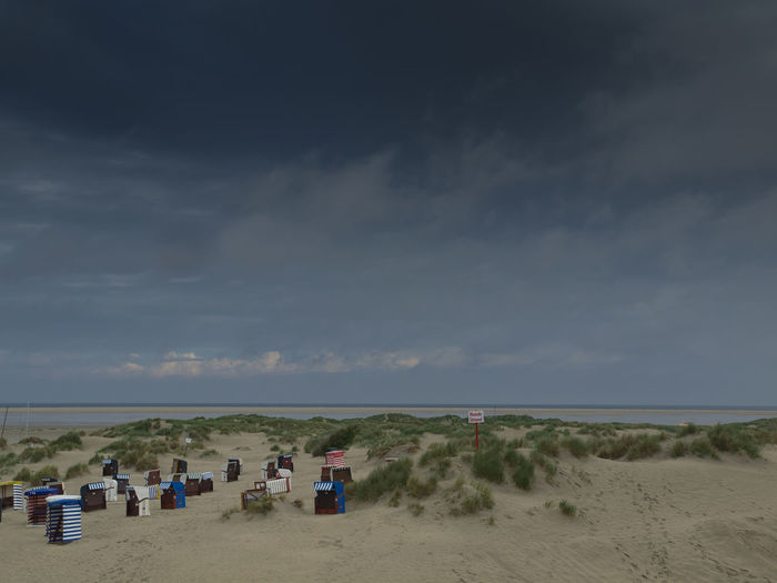 View of hooded chairs on beach against cloudy sky