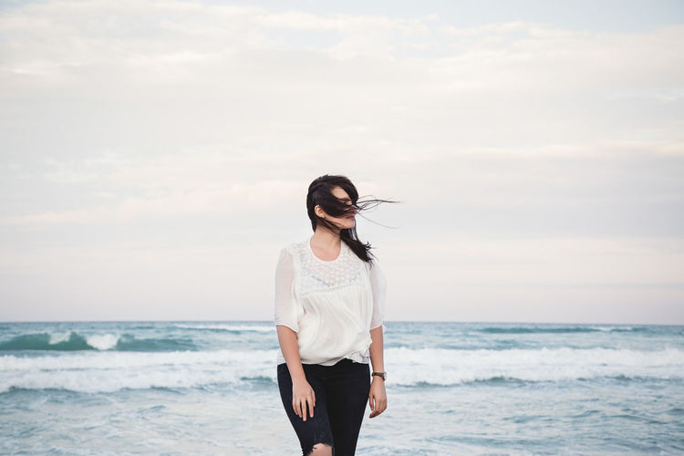 Portrait of a young beautiful woman with windy hair standing by the sea