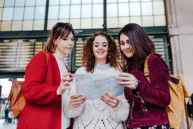 Cheerful women holding map while standing outdoors