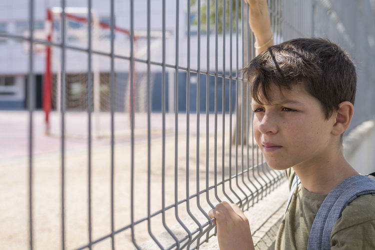 Boy standing by fence in schoolyard