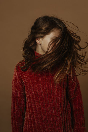Girl tossing hair while standing against brown background