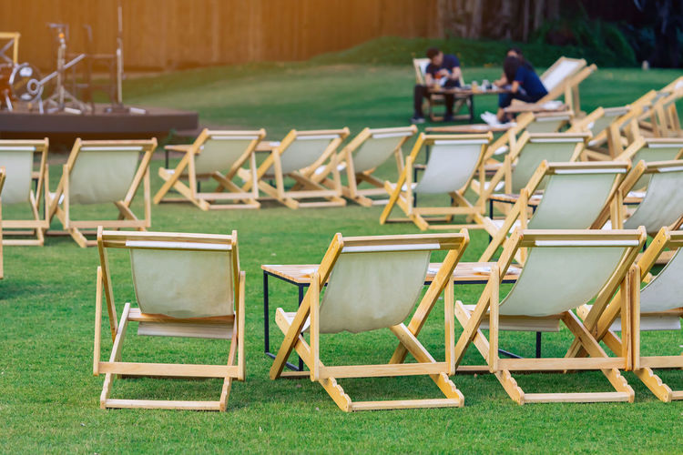 Many white deck chairs with tables for dinner in lawn is surrounded by shady green grass 
