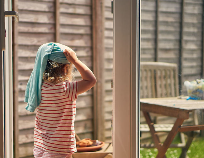Rear view of girl standing against window at home