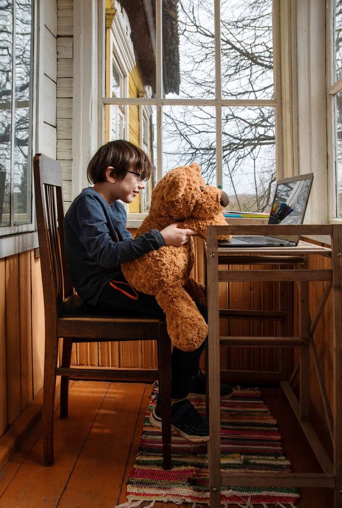 Kid sitting on chair, holding toy bear, looking at computer