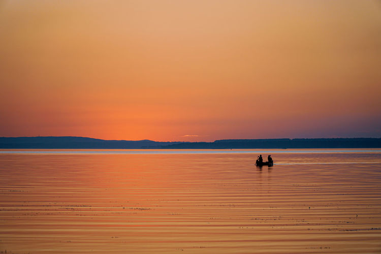 Silhouette people on boat in sea against orange sky