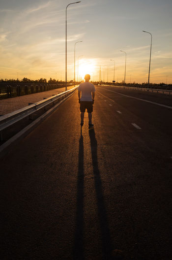 Rear view of man standing on road against sky during sunset