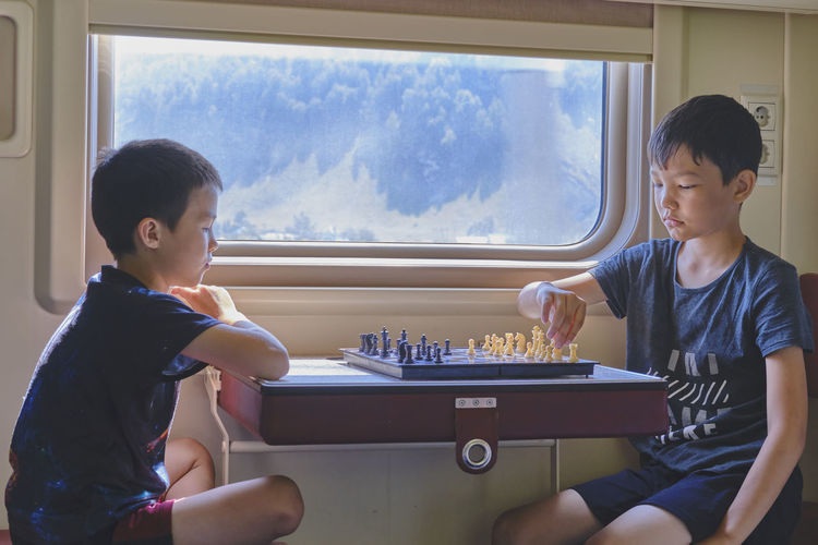 Young boys playing chess near window in train travel, table games concept