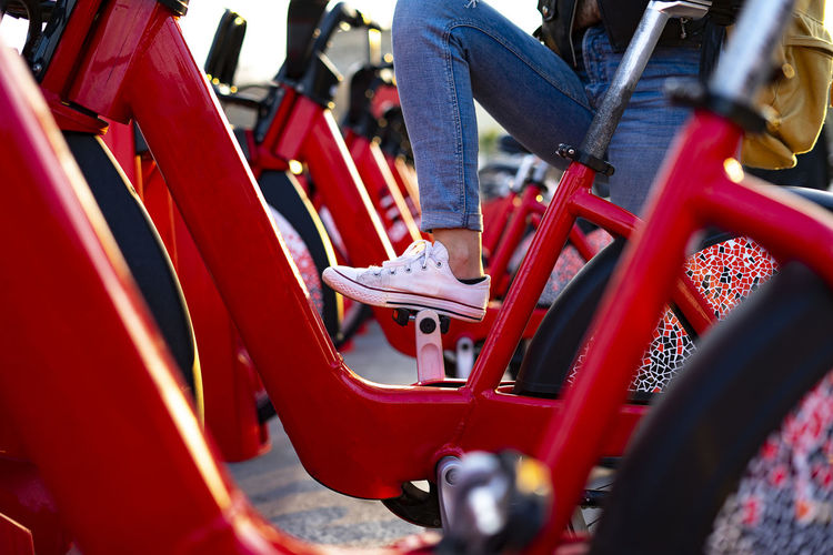 Foot climbing on a pedal of a red bike at a bike rental station.
