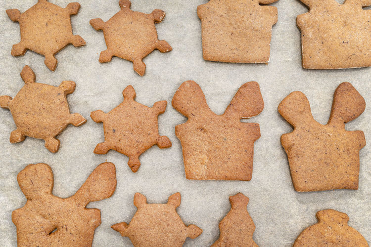 Baked gingerbread cookies in various shapes without decorations, lying on baking paper, top view.
