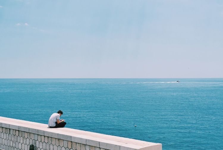 Man sitting on sea against sky