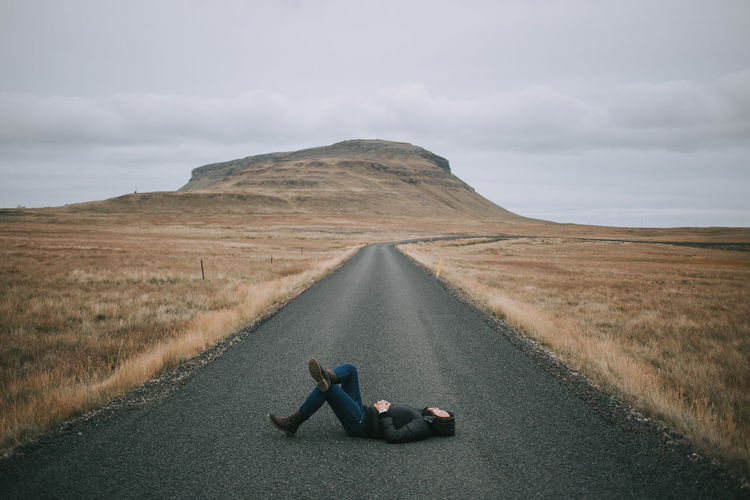 Woman lying on road against sky
