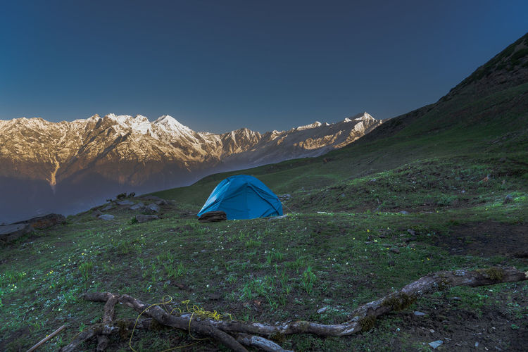 Tent on land by mountain against clear blue sky
