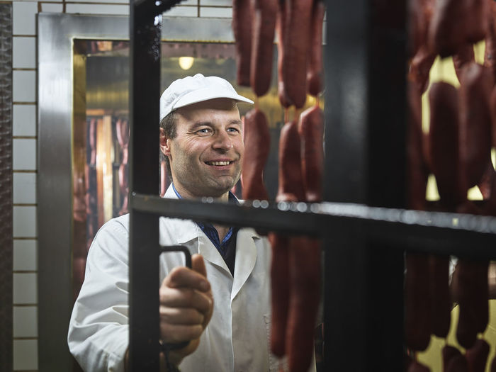 Smiling butcher pulling sausages out of smokehouse at butchery