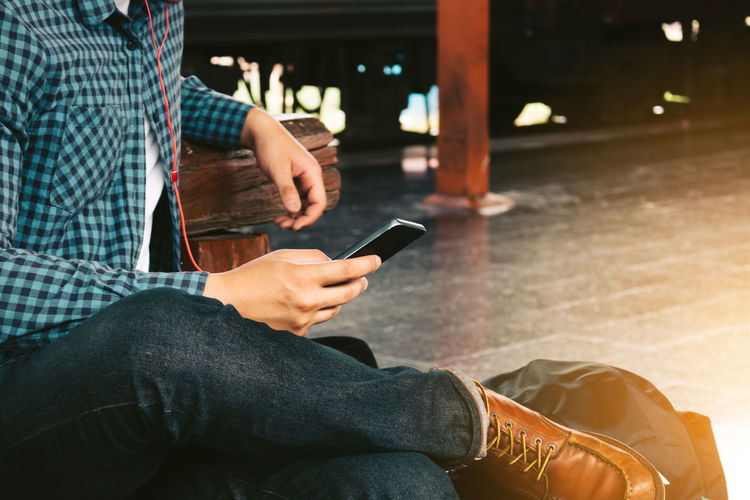 Low section of man using smart phone sitting at station