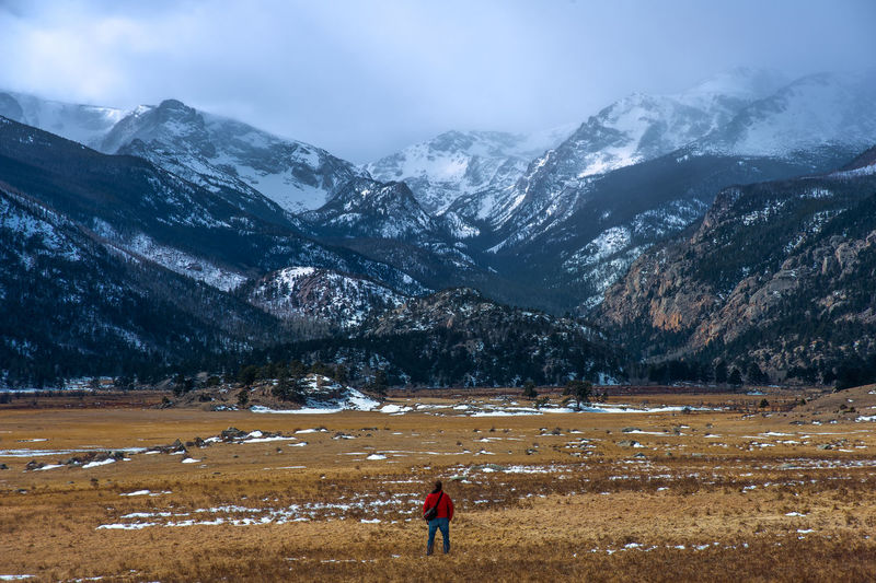 Rear view of man walking on field against snowcapped mountains