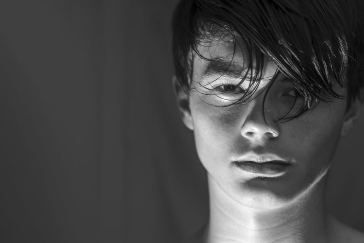 Close-up portrait of shirtless boy against black background