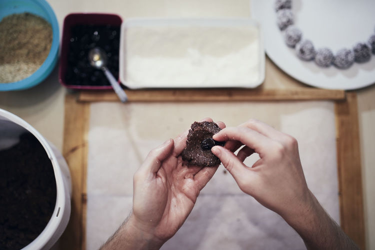 Hands holding cocoa dough and raisin on background work table with other ingredients. 