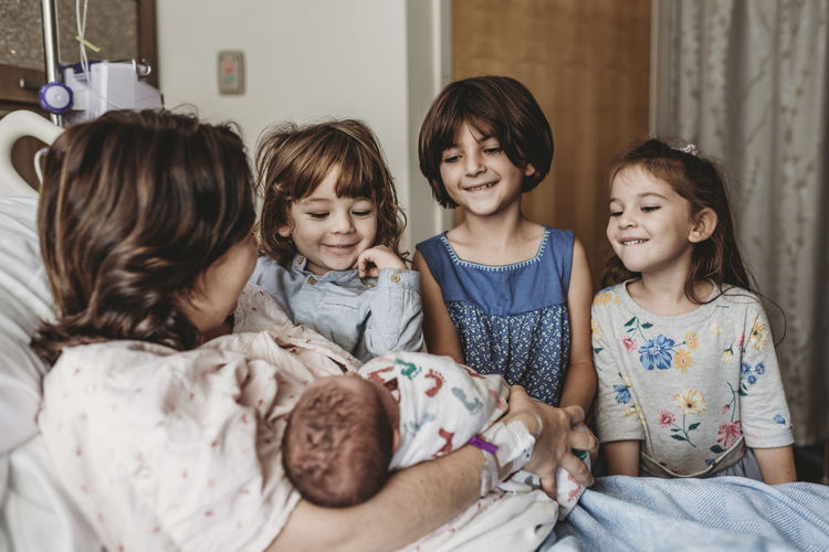 Side view of mother holding newborn son meeting siblings