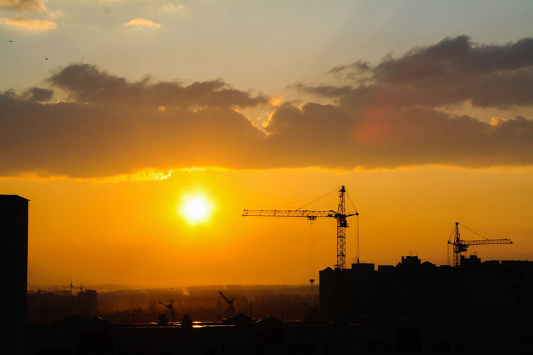 Silhouette cranes at construction site against romantic sky during sunset
