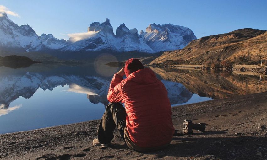 Rear view of man sitting on rock against lake