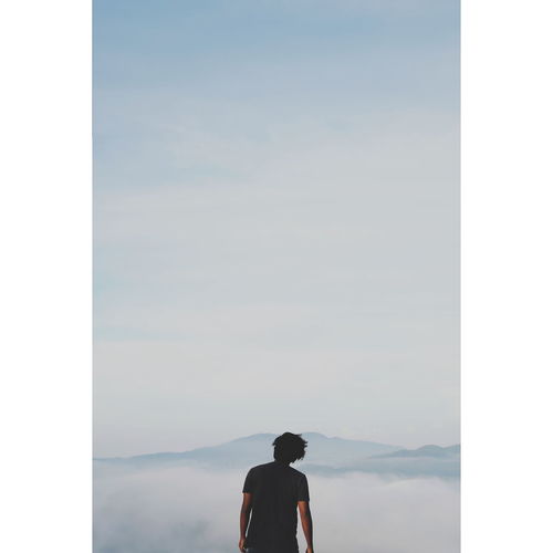 Rear view of man standing on mountain against sky