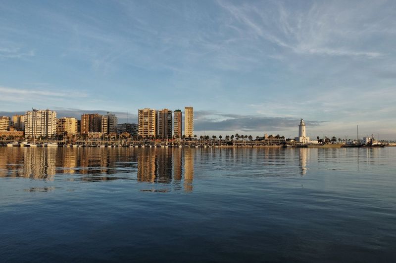 Wooden posts on sea by buildings in city against sky, malaga - spain