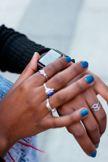From above of crop anonymous black female wearing rings on manicured fingers with blue nail polish touching wristwatch