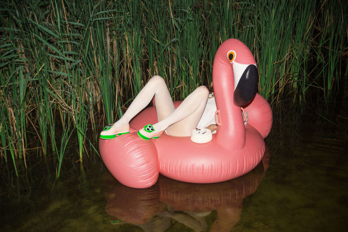 Low section of woman in flamingo inflatable ring on pond