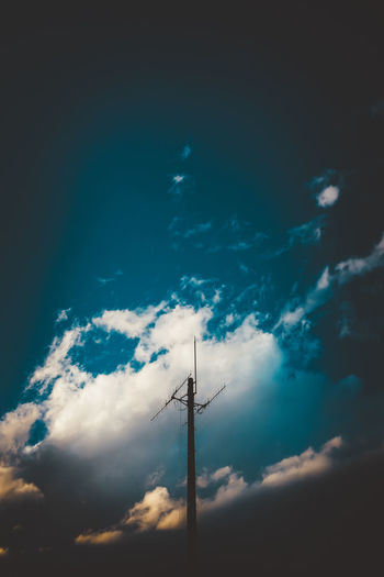 Low angle view of silhouette communications tower against blue sky