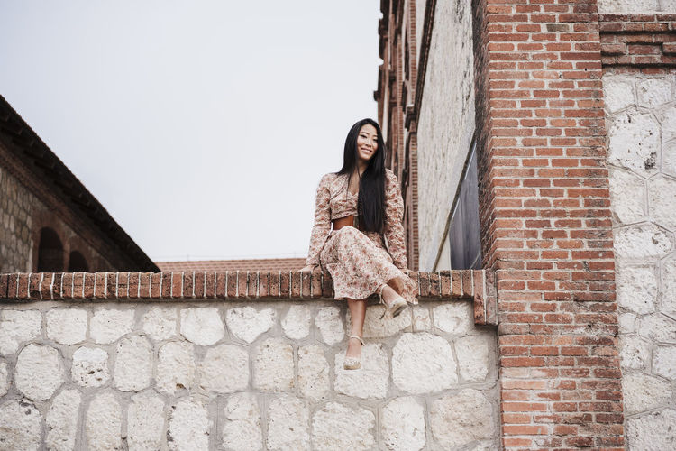 Carefree woman sitting on retaining wall in city