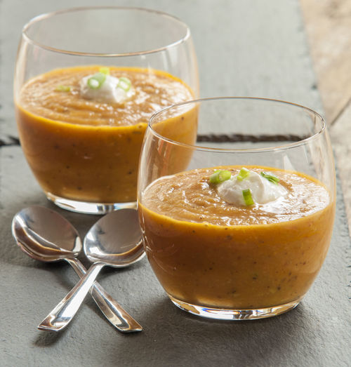 Close-up of pumpkin cream soup in glass by spoons on table