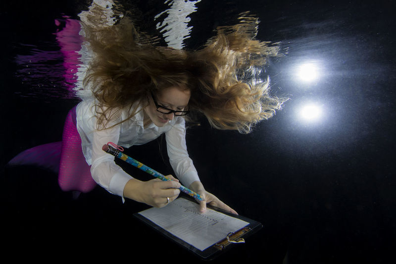 Smiling young mermaid woman writing while swimming underwater