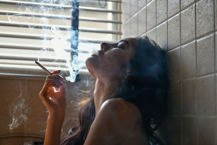 Woman smoking cigarette against wall