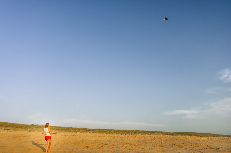 Woman flying kite while standing on field against sky