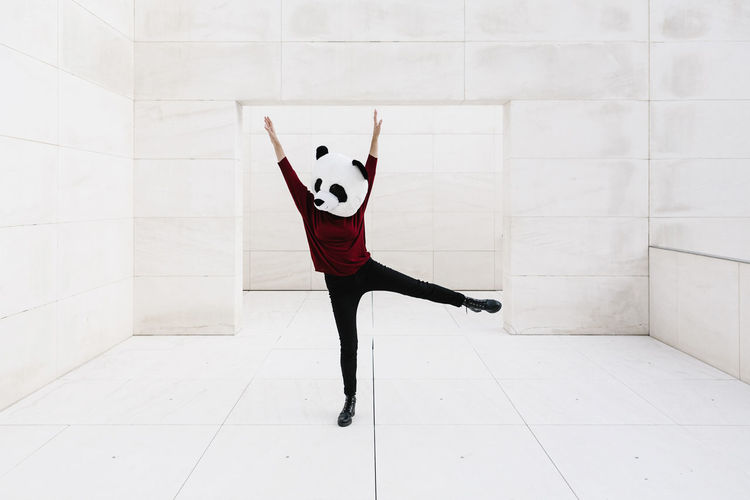 Woman wearing panda mask with arms raised standing against doorway