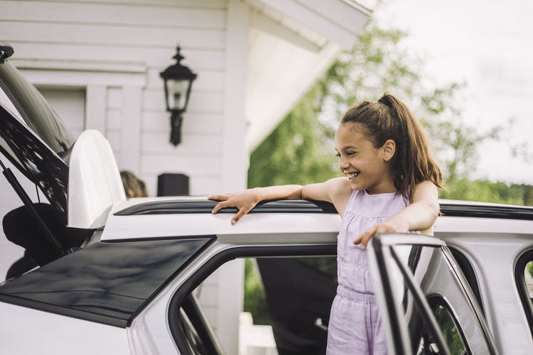 Happy elementary girl leaning on electric car door