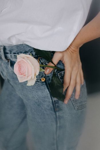 Midsection of woman with rose in jeans pocket