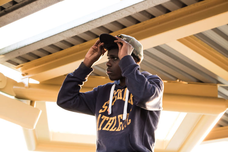 Young man wearing cap while looking away against ceiling