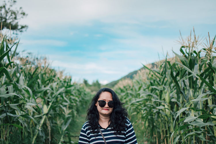 Portrait of mid adult woman standing by plants against sky