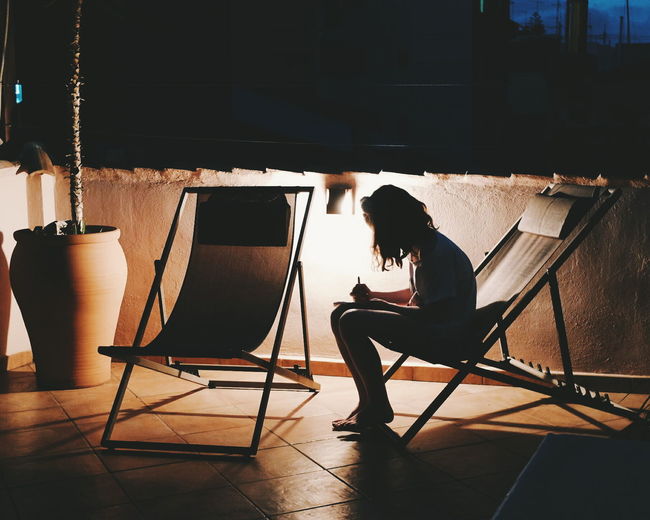 Woman sitting on deck chair against illuminated lighting equipment