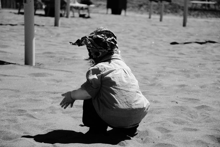 Rear view of baby girl crouching on sand at beach during sunny day