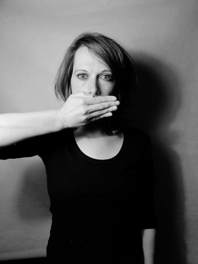 Portrait of woman covering mouth while standing against wall