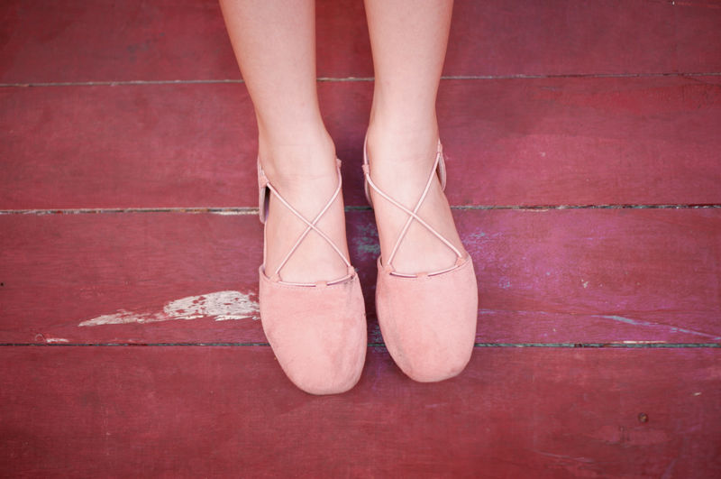 Low section of woman wearing shoes on wooden floor