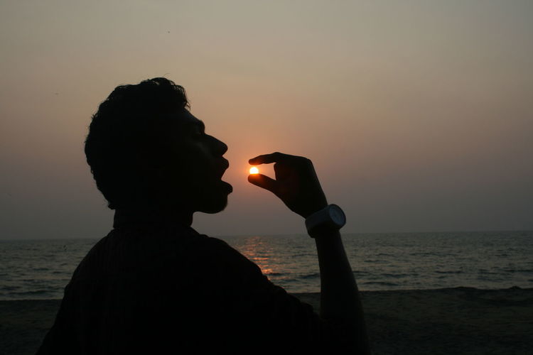 Optical illusion of silhouette men eating sun at sunset
