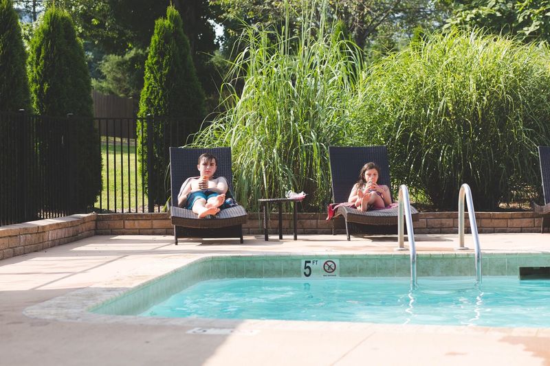 Siblings relaxing on chairs at poolside