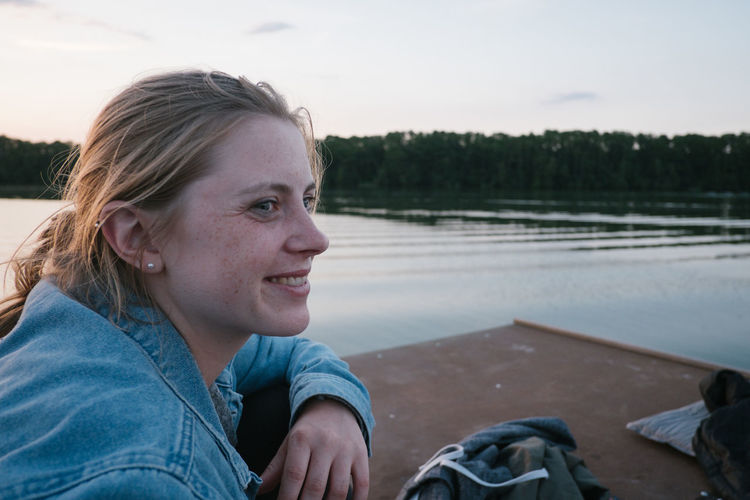 Smiling woman looking away while sitting by lake