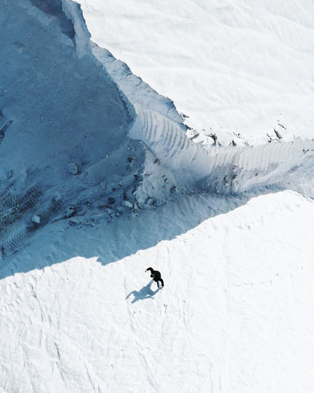 HIGH ANGLE VIEW OF PERSON SKIING ON SNOWCAPPED MOUNTAINS