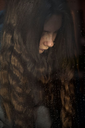 Young girl stay at home, near the window on which raindrops. autumn mood, self isolation, loneliness