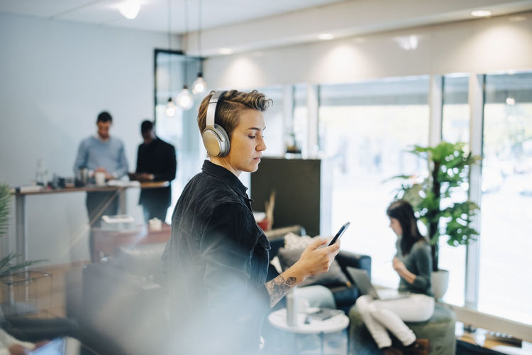 Female entrepreneur using smart phone while colleagues working in background